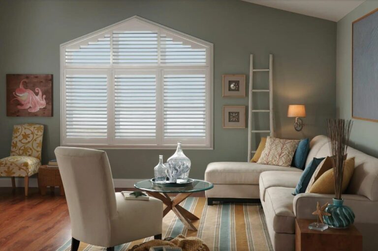 Custom window blinds in a modern coastal-themed living room featuring white plantation shutters on an angled window