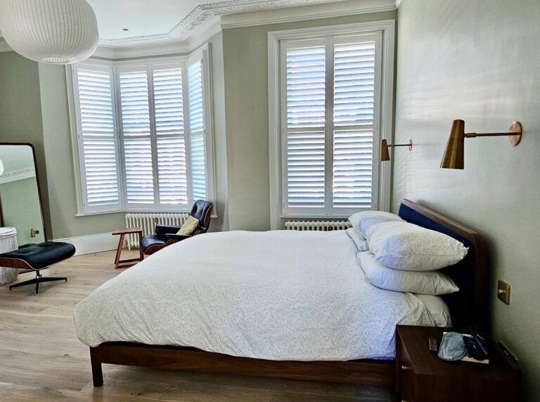 Bright bedroom featuring custom made-to-order shutters in white, with bay window plantation shutters and modern brass wall lights