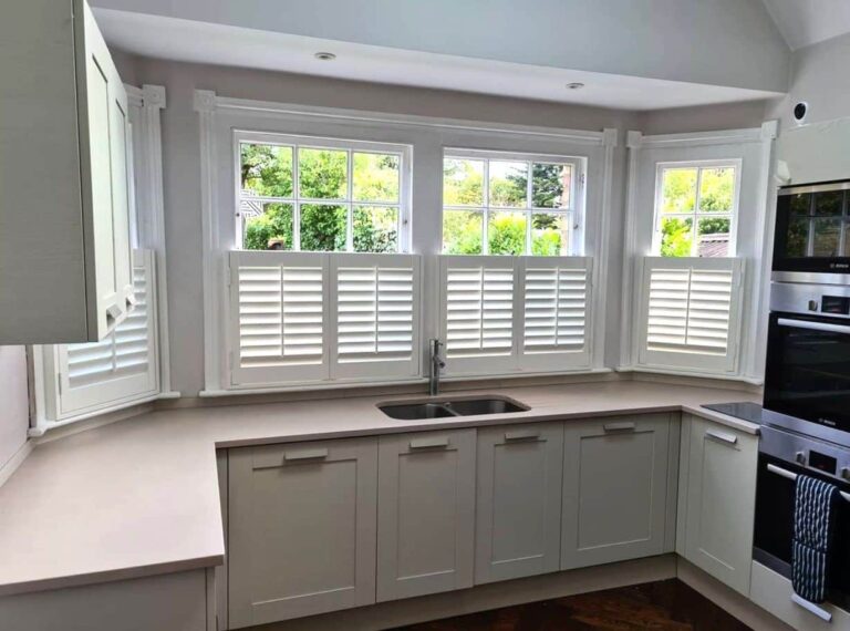 Durable bamboo window shutters installed in a bright kitchen with white cabinetry and a corner sink