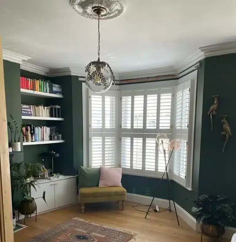 Hexagonal window shutters with white panels in a green-themed living room, showcasing North London Shutters and Blinds' craftsmanship.