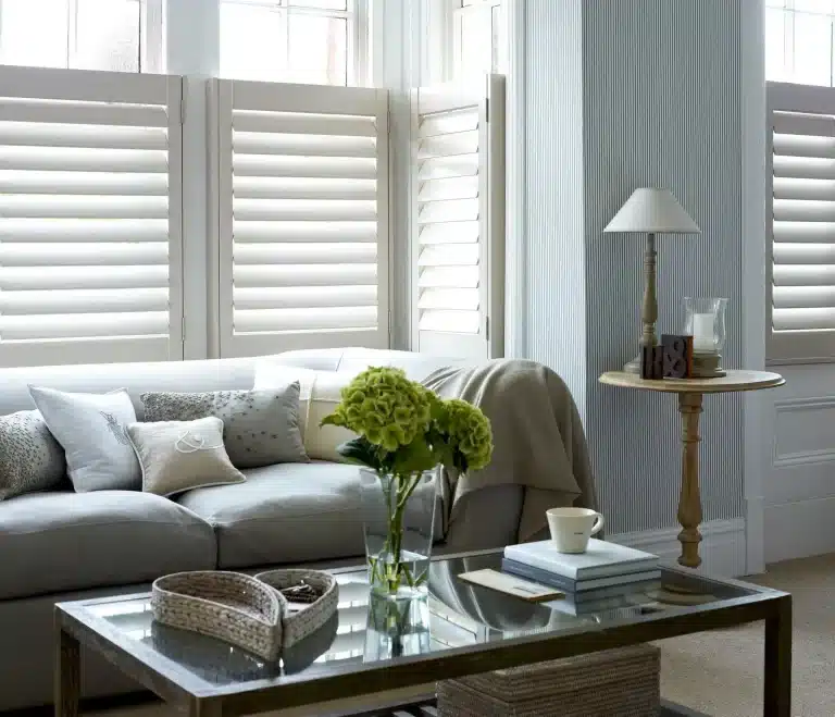 Modern living room featuring white satin finish shutters, grey sofa, green hydrangeas, and contemporary decor