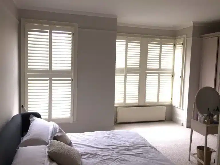 Bedroom with natural wood shutters installed on windows, enhancing the aesthetic and functionality of the space.