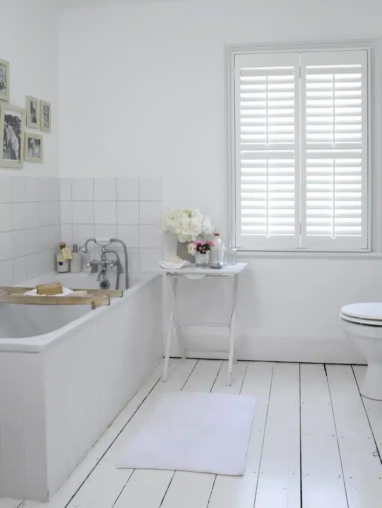 Bright bathroom interior with red wooden shutters featuring white painted floorboards and classic bathtub