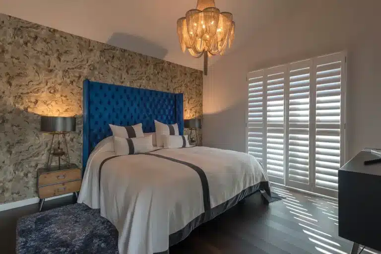 Stylish bedroom featuring beige wooden shutters, a blue tufted headboard, and modern decor.