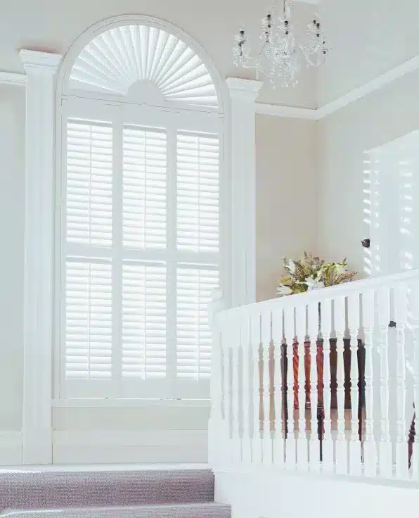 Custom colour shutters in white featuring an arched window design with sunburst detail and crystal chandelier