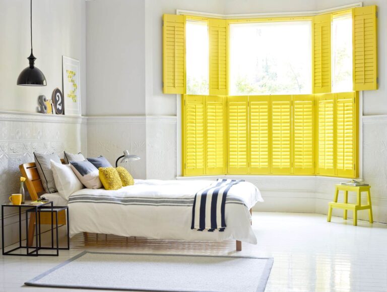 Stylish yellow shutters from a window store enhance this contemporary bedroom's natural light and design.