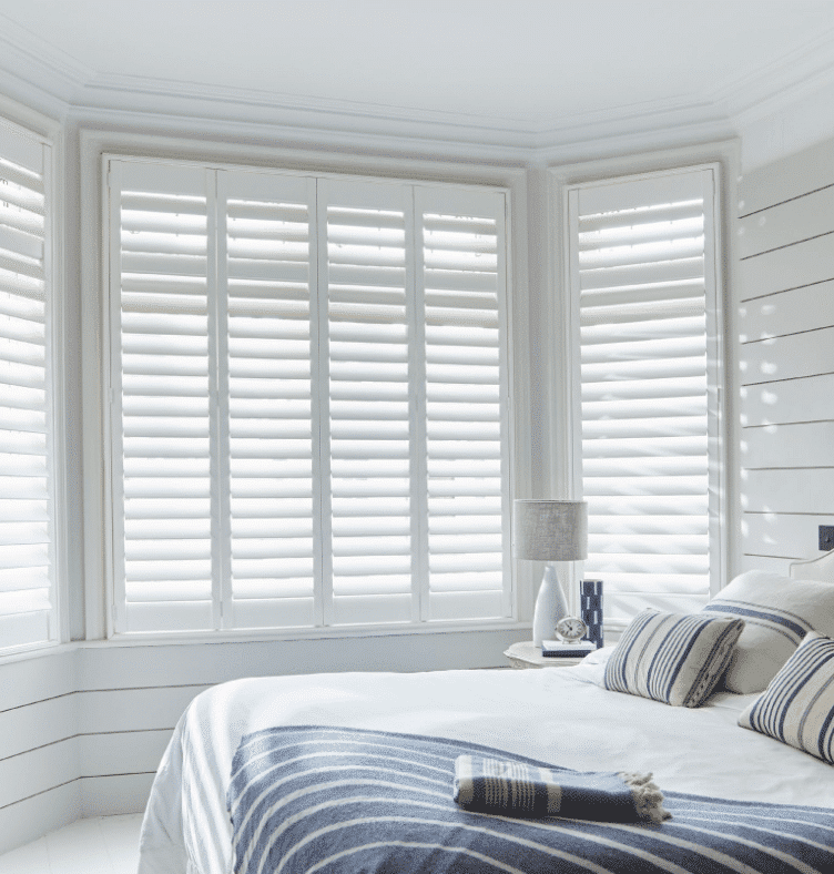 Bright white made-to-measure shutters installed on a bay window in a contemporary bedroom, providing privacy and light control