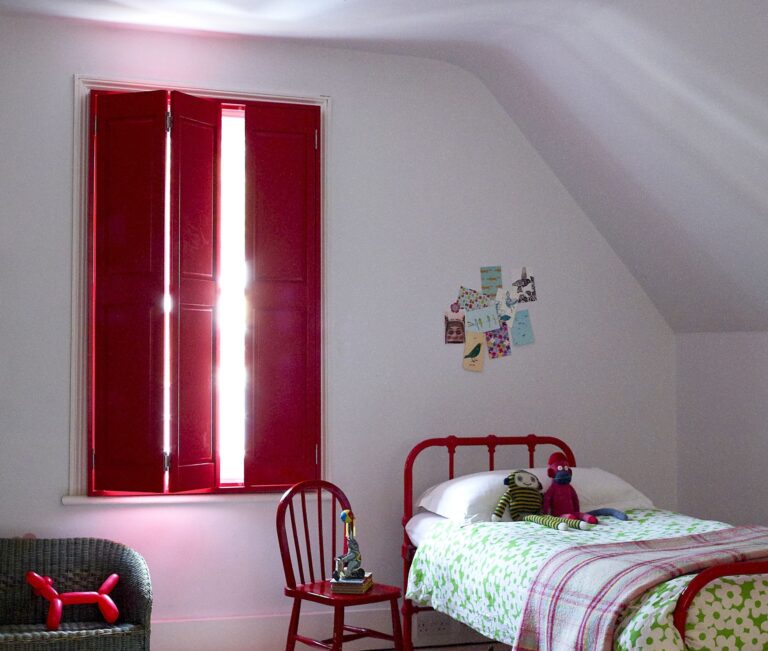 Red window shutters in a bedroom setting showcasing handcrafted design from North London Shutters and Blinds
