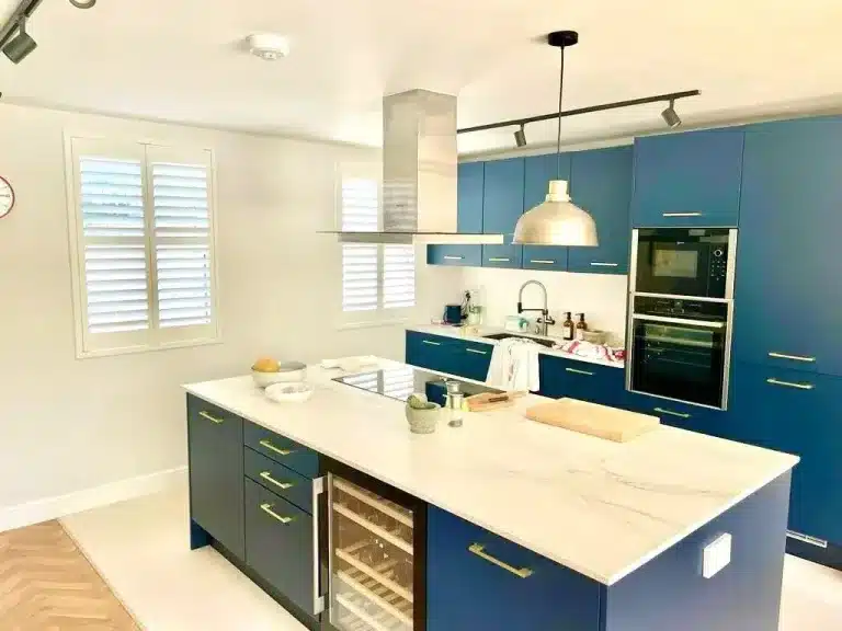 Contemporary kitchen featuring blue cabinets and wooden shutter interior window treatments by North London Shutters and Blinds