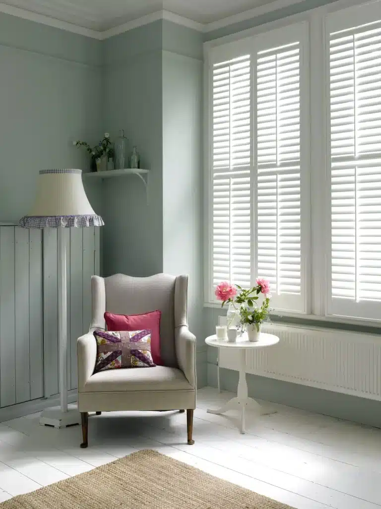 Bright living room with white interior wooden plantation shutters, featuring a cozy armchair and minimalist decor