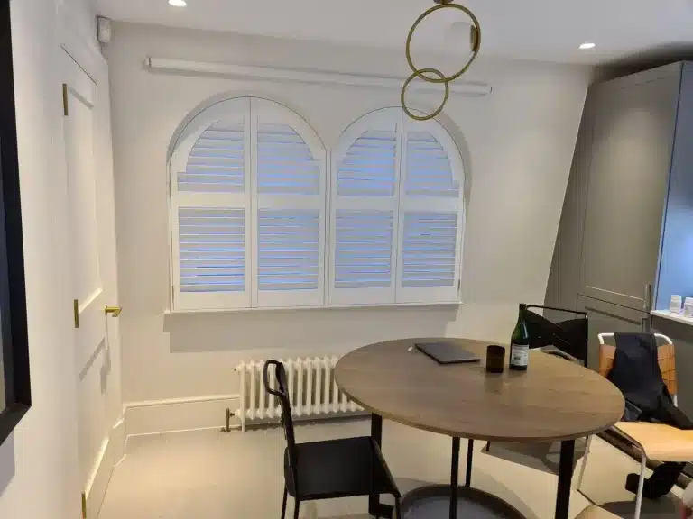 Custom white wood shutters interior with arched windows enhancing a minimalist London home office space