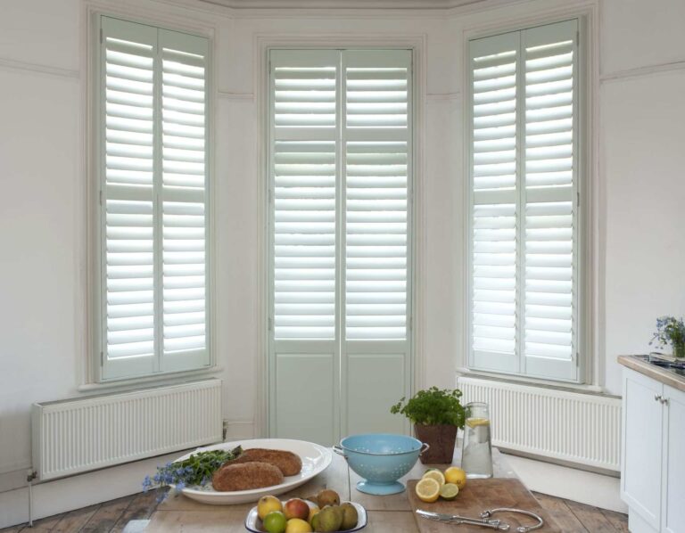 Beautiful white made to measure shutters installed in a bright bay window dining area, showcasing custom plantation shutters from North London Shutters and Blinds