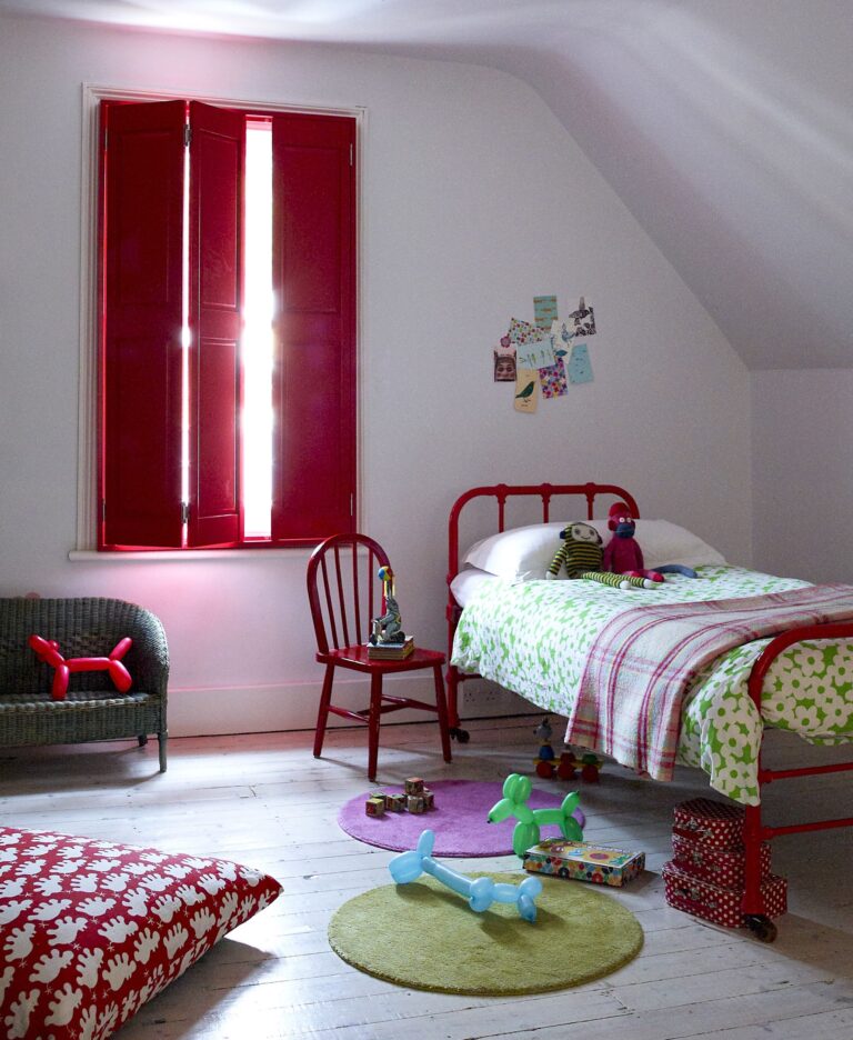 Complete shutters in burgundy red color installed in child's attic bedroom with matching red furniture and decor