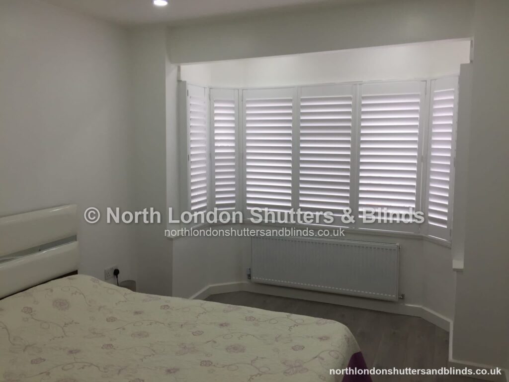 White full height plantation shutters on a bay window in a bedroom by shutter fitters in Barnet, North London