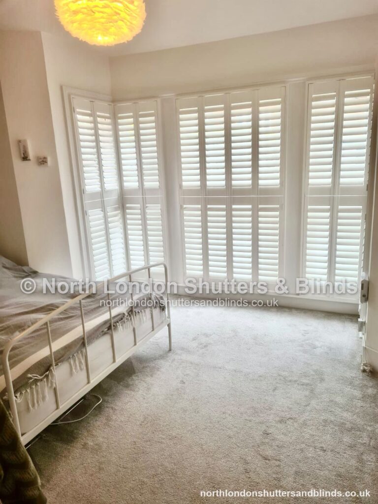 White full height plantation shutters on a bay window in a bedroom by shutter fitters in Barnet, North London