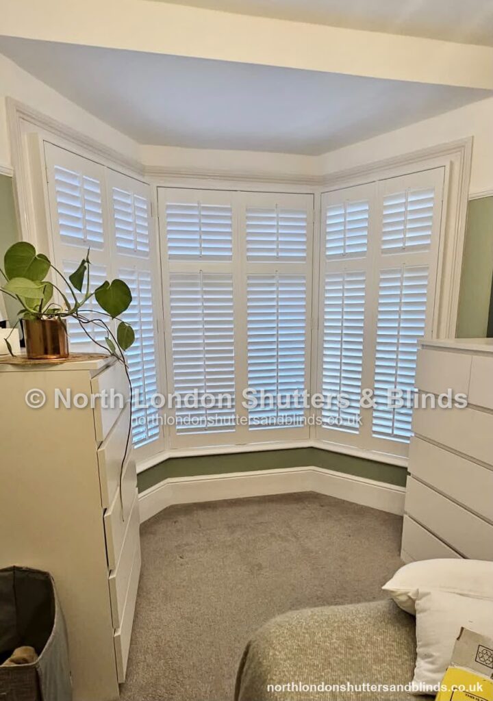 White full height plantation shutters on a bay window in a bedroom by shutter fitters in Barnet, North London