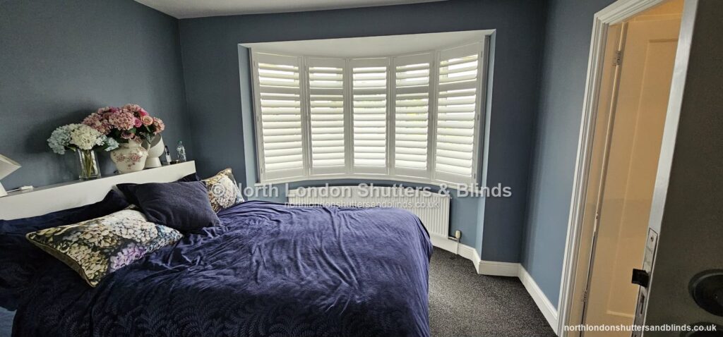 White full height plantation shutters on a bay window in a bedroom by shutter fitters in Barnet, North London
