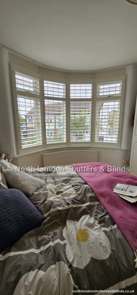 White full height plantation shutters on a bay window in a bedroom by shutter fitters in Barnet, North London