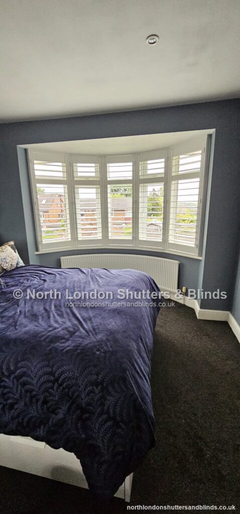White full height plantation shutters on a bay window in a bedroom by shutter fitters in Barnet, North London