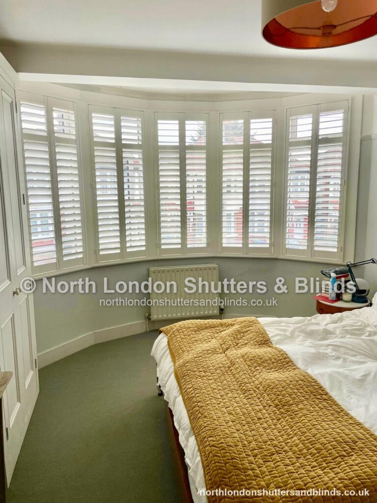 White full height plantation shutters on a bay window in a bedroom by shutter fitters in Barnet, North London