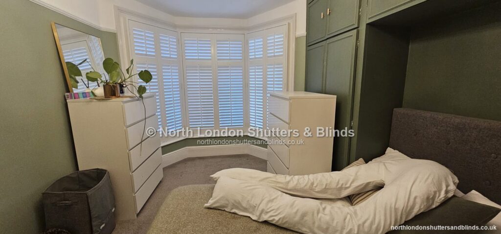 White full height plantation shutters on a bay window in a bedroom by shutter fitters in Barnet, North London