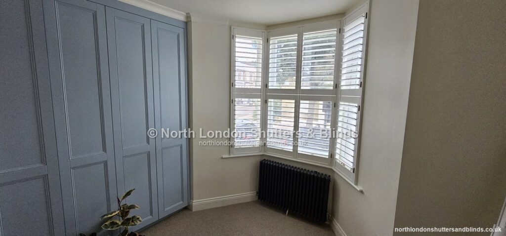 White full height plantation shutters on a bay window in a bedroom by shutter fitters in Barnet, North London