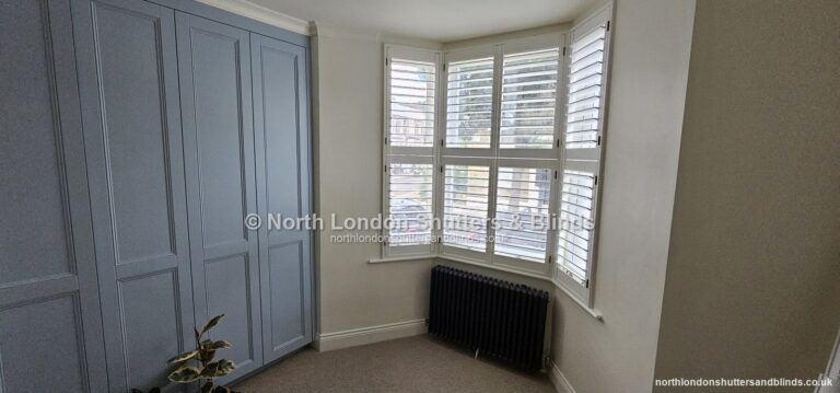 White full height plantation shutters on a bay window in a bedroom by shutter fitters in Barnet, North London