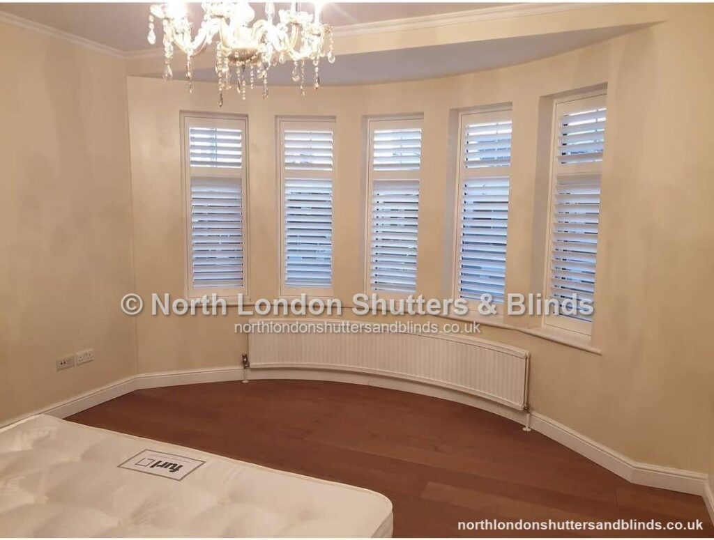 White full height plantation shutters on a curved bay window in a bedroom by shutter fitters in Barnet, North London
