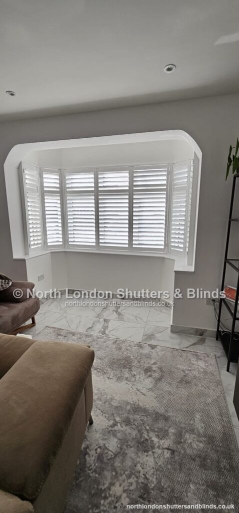 White full height plantation shutters on a curved bay window in a bedroom by shutter fitters in Barnet, North London