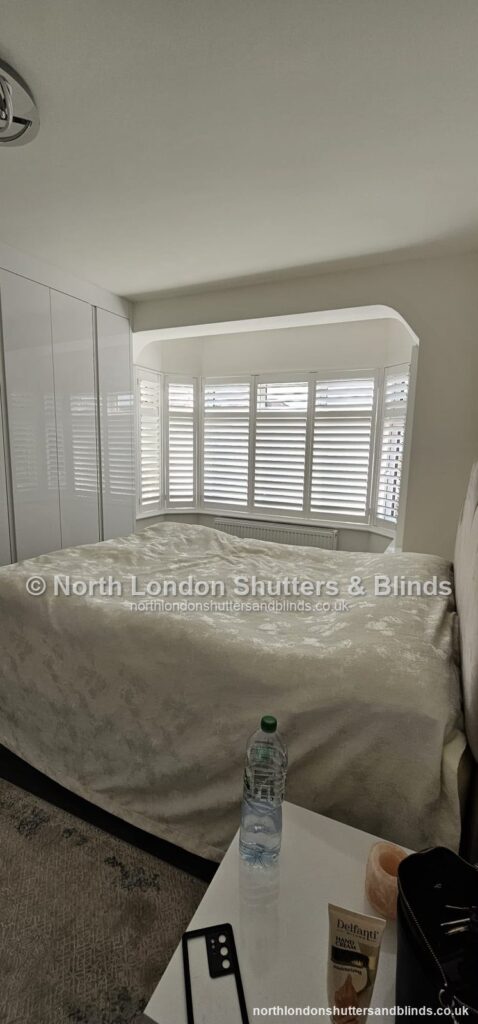 White full height plantation shutters on a curved bay window in a bedroom by shutter fitters in Barnet, North London
