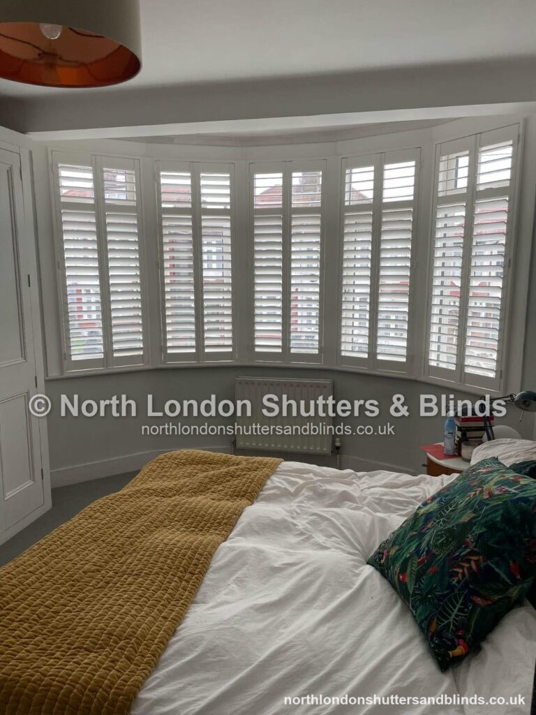 White full height plantation shutters on a large bay window in a bedroom by shutter fitters in Barnet, North London