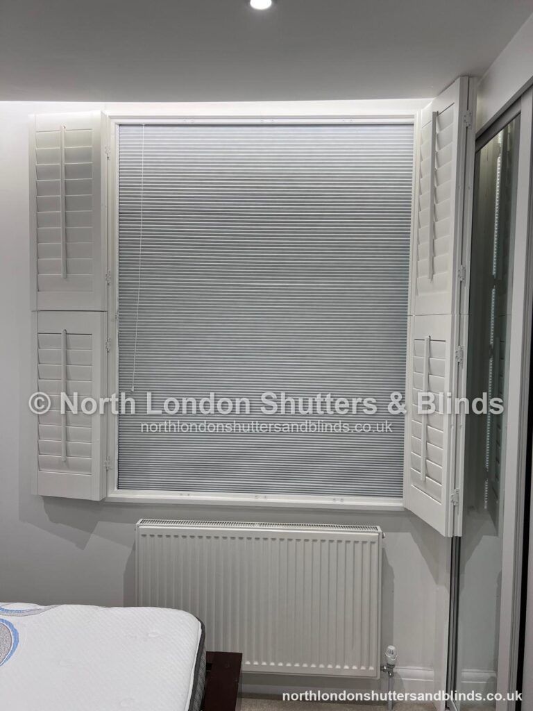 White full height plantation shutters in a bedroom, with a blackout blind behind by shutter fitters in Barnet, North London