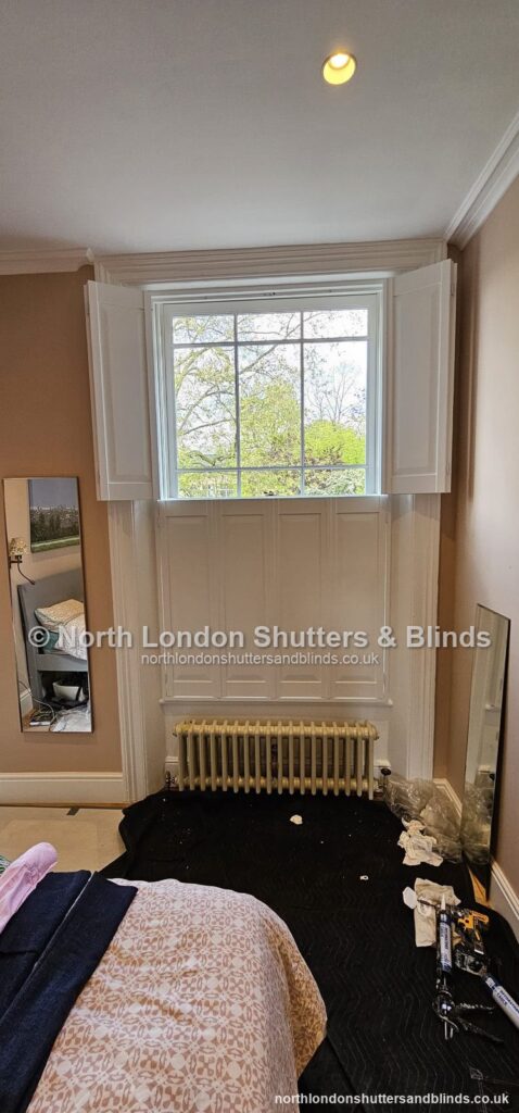 White solid panel shutters on a sash window in a bedroom, with the shutters open by shutter fitters in Barnet, North London