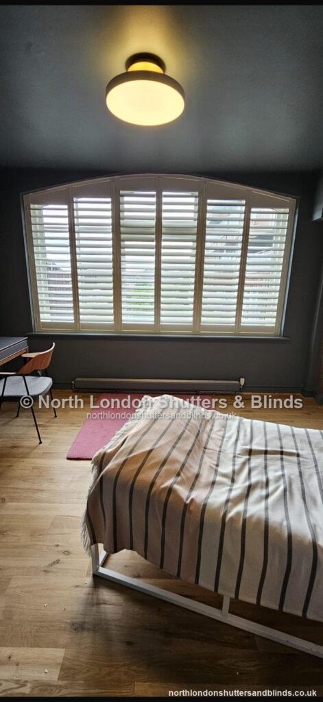 White special shape plantation shutters on an arched window in a bedroom by shutter fitters in Barnet, North London