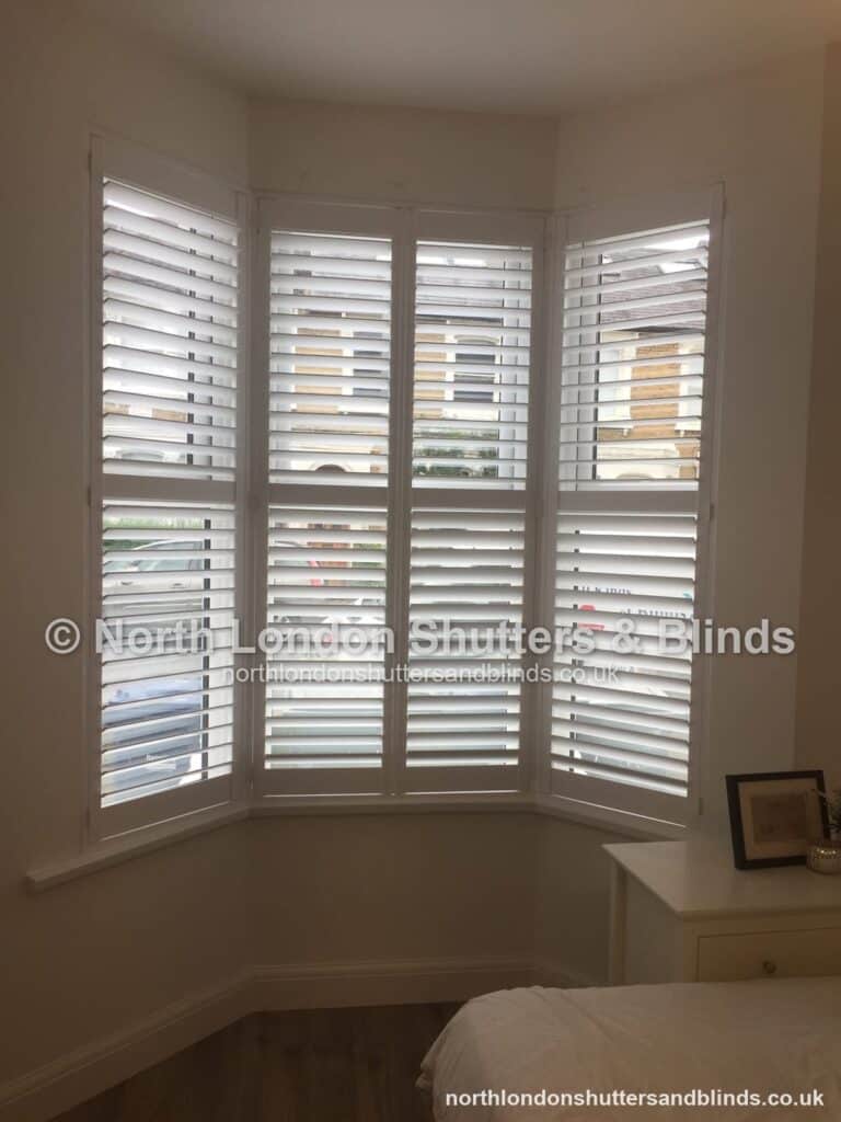 White tier-on-tier plantation shutters on a bay window in a bedroom by shutter fitters in Barnet, North London