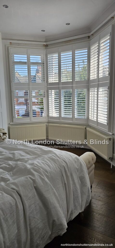White tier-on-tier plantation shutters on a bay window in a bedroom by shutter fitters in Barnet, North London