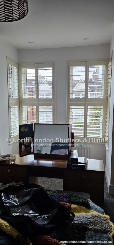 White tier-on-tier plantation shutters on a bay window in a bedroom by shutter fitters in Barnet, North London