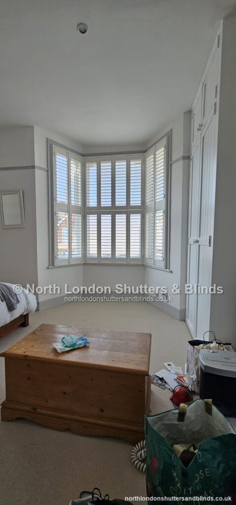 White tier-on-tier plantation shutters on a bay window in a bedroom by shutter fitters in Barnet, North London