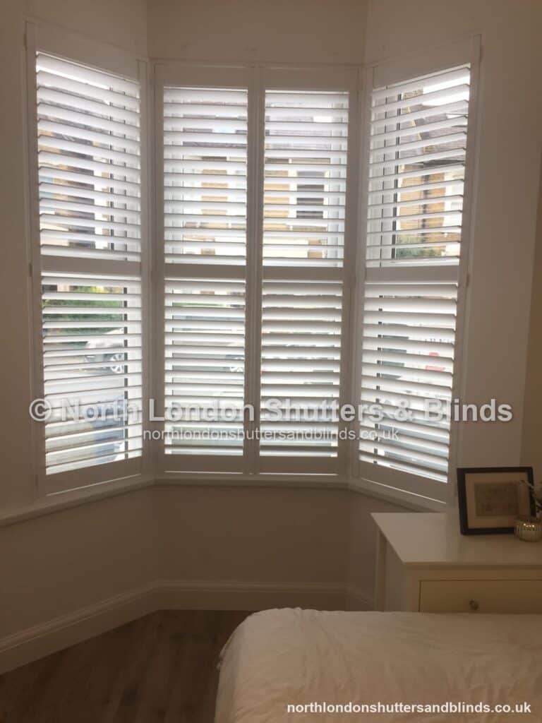 White tier-on-tier plantation shutters on a bay window in a bedroom by shutter fitters in Barnet, North London