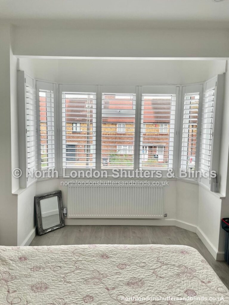 White tier-on-tier plantation shutters on a bay window in a bedroom by shutter fitters in Barnet, North London