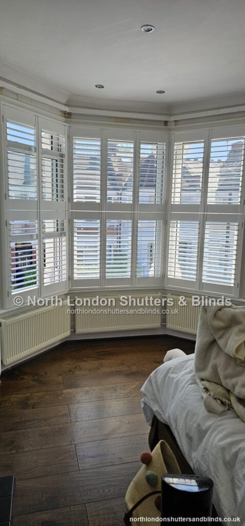 White tier-on-tier plantation shutters on a bay window in a bedroom by shutter fitters in Barnet, North London