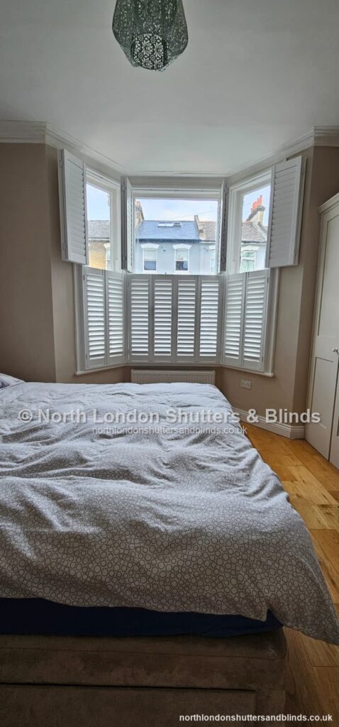 White tier-on-tier plantation shutters on a bay window in a bedroom by shutter fitters in Barnet, North London