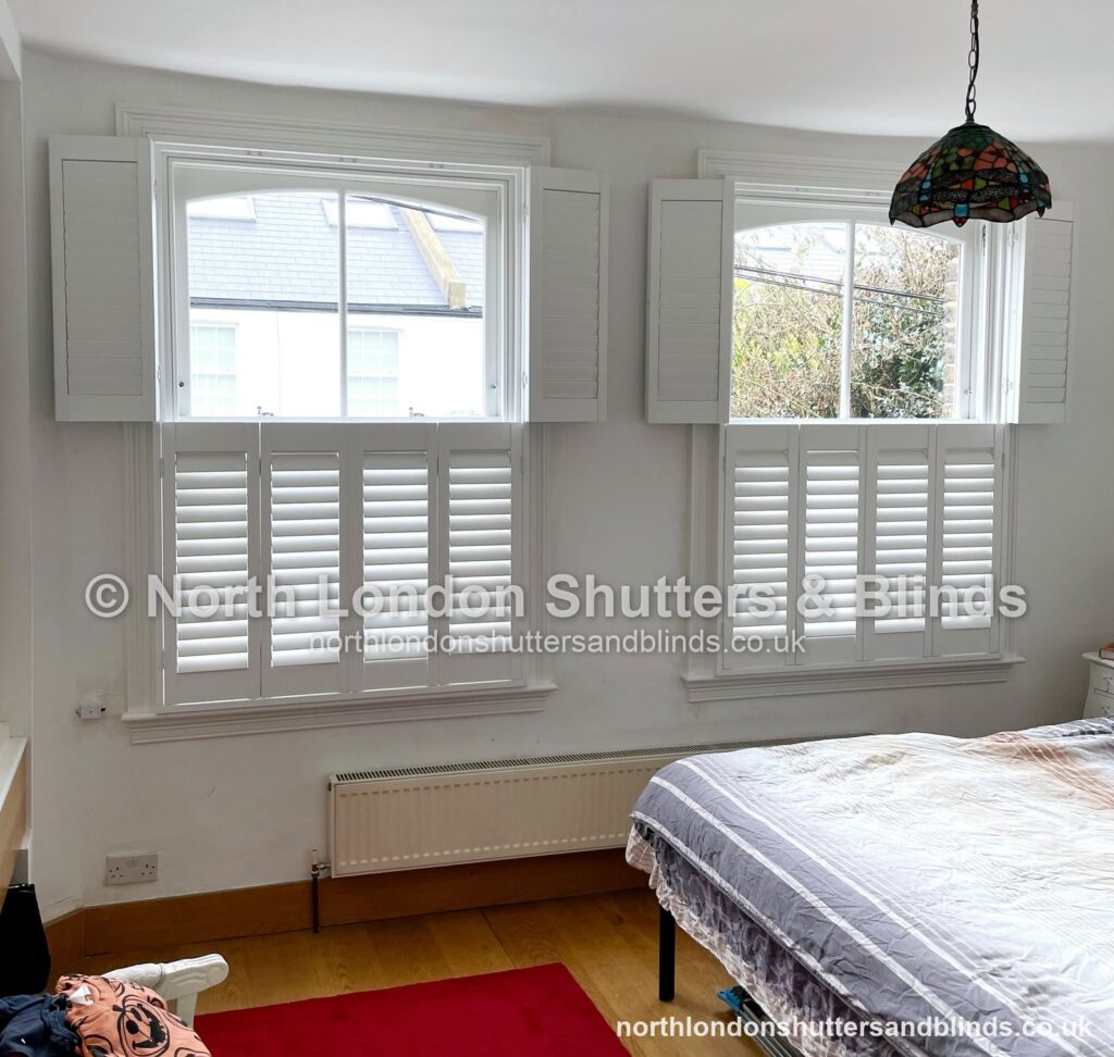 White tier-on-tier plantation shutters on two windows in a bedroom by shutter fitters in Barnet, North London