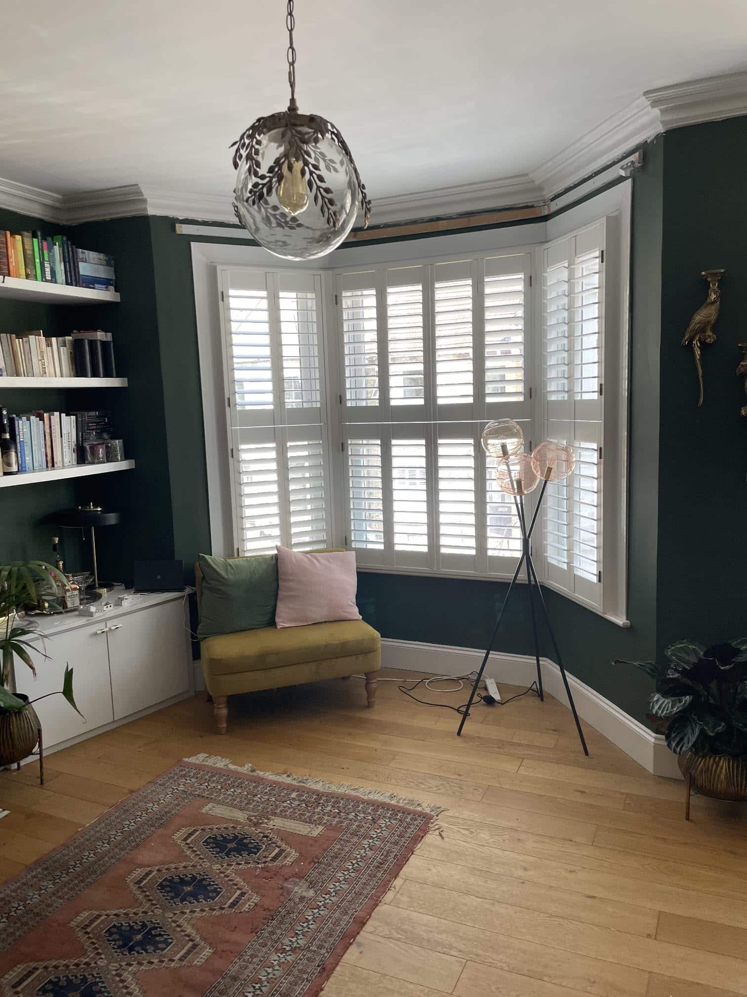 White wooden shutters on a bay window in a dark green North London living room
