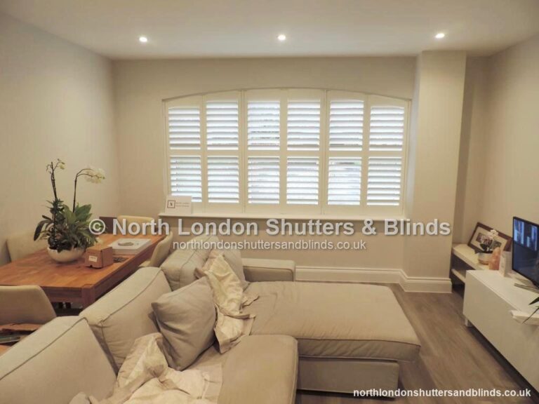White special shape plantation shutters on an arched-top window in a living room by shutter fitters in Barnet, North London