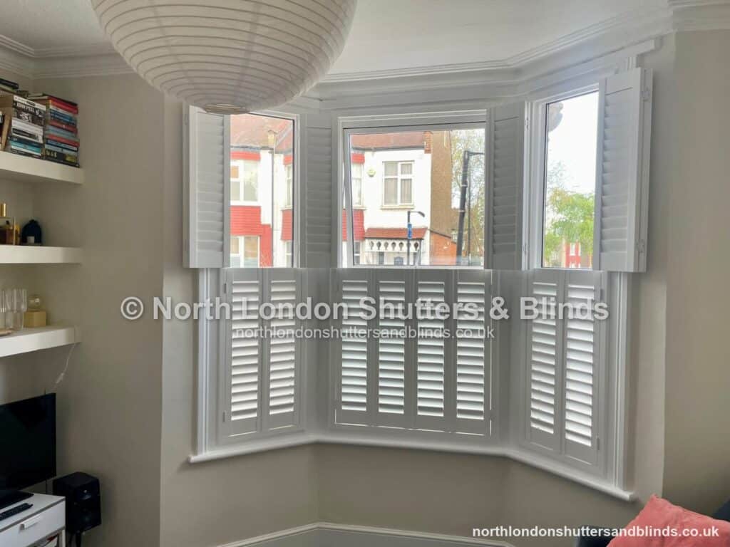 White tier-on-tier plantation shutters on a bay window in a living room by shutter fitters in Barnet, North London