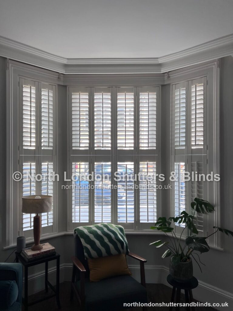 White tier-on-tier plantation shutters on a bay window in a living room by shutter fitters in Barnet, North London