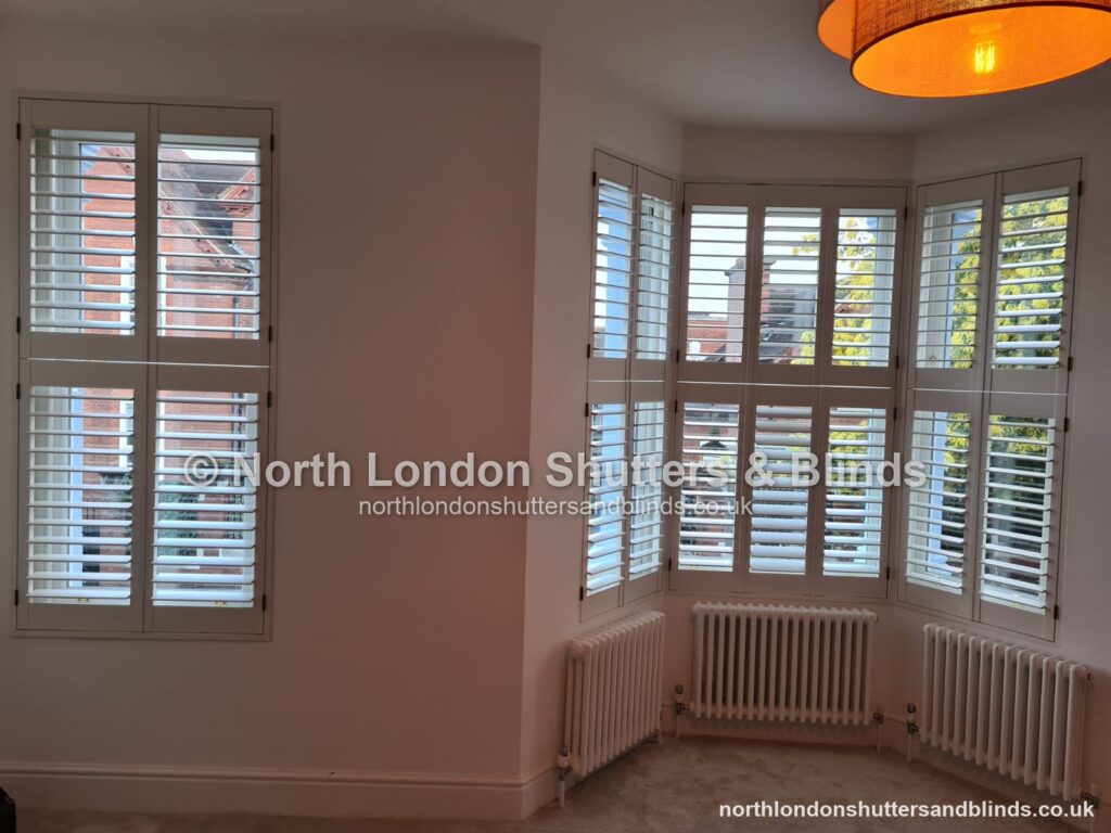 White tier-on-tier plantation shutters on a bay window in a living room by shutter fitters in Barnet, North London