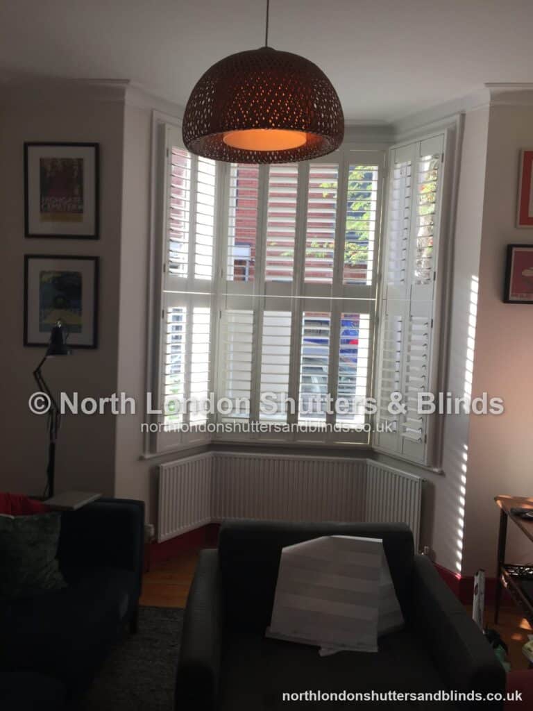 White tier-on-tier plantation shutters on a bay window in a living room by shutter fitters in Barnet, North London