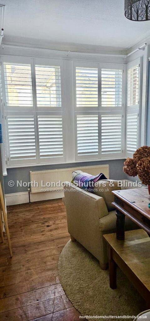 White tier-on-tier plantation shutters on a bay window in a living room by shutter fitters in Barnet, North London